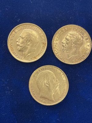 three gold sovereign coins on a blue cloth