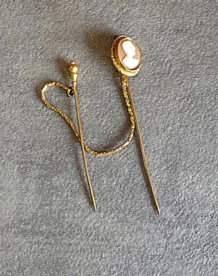 deux épingles à cheveux dorées ornées de perles et de chaînes, posées sur un fond gris