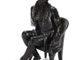 statue of a man sitting in a chair with his legs crossed