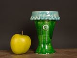 a green vase next to an apple on a table