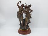 statue en bronze représentant deux femmes tenant un oiseau, posée sur un socle en bois