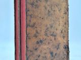 an old book with a red cover sitting on a white surface