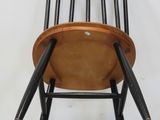 a wooden chair with black legs against a white wall