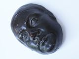 une sculpture noire représentant le visage d'un homme sur une surface blanche