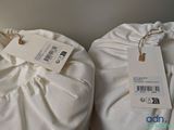two white bags with tags on them sitting on a bed