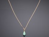a gold necklace with a green tear shaped stone hangs from a gold chain