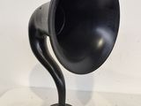 un vieux gramophone noir posé sur un socle en bois, lui-même posé sur une surface blanche