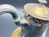a silver tea pot with a handle on a table