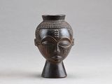 un vase noir orné d'un visage, posé sur une table