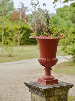 un vase rouge contenant des plantes, posé sur un socle en pierre