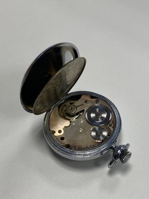 une montre de poche en argent posée sur une surface blanche