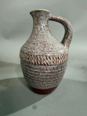 un vase marron et blanc muni d'une anse, posé sur une table