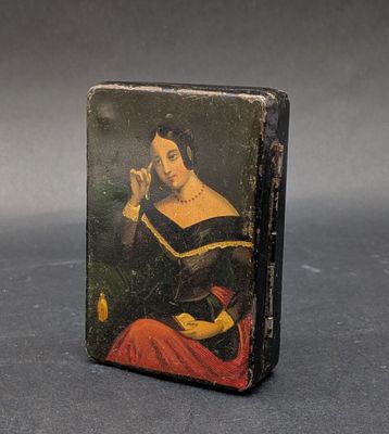 une vieille boîte noire sur laquelle est peinte une femme assise sur une chaise