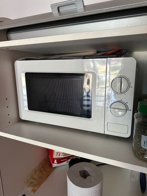 a white microwave on a shelf with a roll of toilet paper