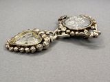 two pieces of silver jewelry sitting on top of a gray surface