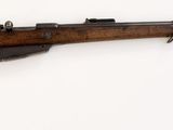 fusil posé sur une surface blanche, muni d'une crosse en bois et d'une poignée en métal