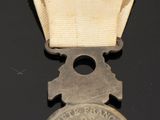 an old silver medal on a black surface with a small piece of paper