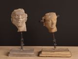 two sculptures of heads on a wooden stand on a table