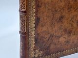 an old leather book with gold trim sitting on top of a white surface
