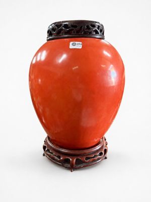 un vase rouge muni d'un couvercle noir, posé sur un socle