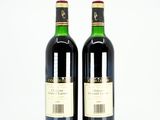 two bottles of red wine sitting next to each other on a white surface
