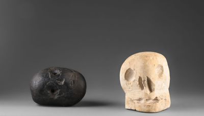 deux crânes en pierre et un rocher posés sur une surface grise