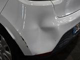 the rear end of a white car with a dent in it ' s bumper