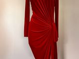 La robe est rouge, elle a des manches longues et un drapé sur le côté.
