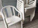 plusieurs chaises en plastique blanc posées sur un sol carrelé à côté d'une porte