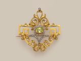 a gold and diamond broochle with a green stone in the center