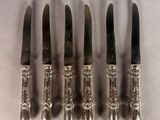 six silverplated knives are lined up in a row on a white surface