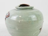 a green vase with a brown lid on a white surface