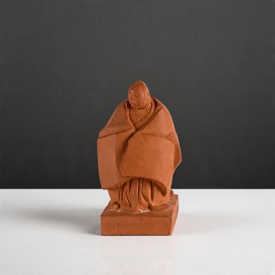 une photo d'une statue en argile représentant un moine, posée sur une table blanche
