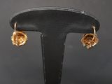 gold plated flower earrings on a black stand against a gray background