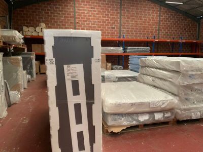 Des cartons contenant des matelas sont empilés sur des palettes dans un entrepôt