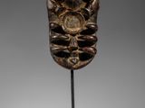 un masque en bois posé sur un socle, sur une surface blanche