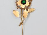 une image représentant une broche en forme de fleur dorée et verte sur fond blanc