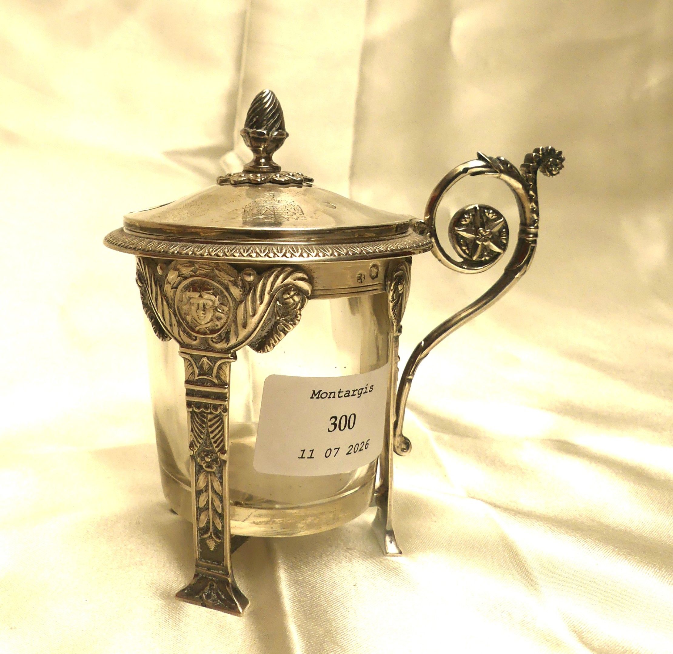 Moutardier en argent à tripode à colonnes à décor de masques, de feuilles et de boutons. Avec un réceptacle en verre....