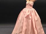 une poupée Barbie en robe rose, avec des gants blancs et une rose