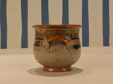 a brown vase sitting on a table with a striped wall behind it