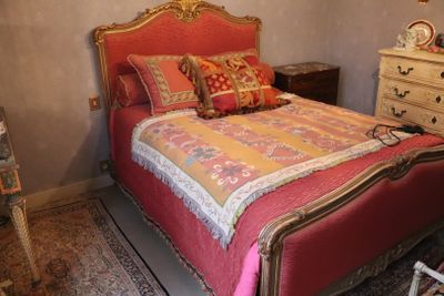 a bed with a red and gold bed spread and pillows on it