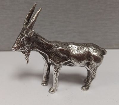 une figurine de chèvre en argent posée sur une surface blanche