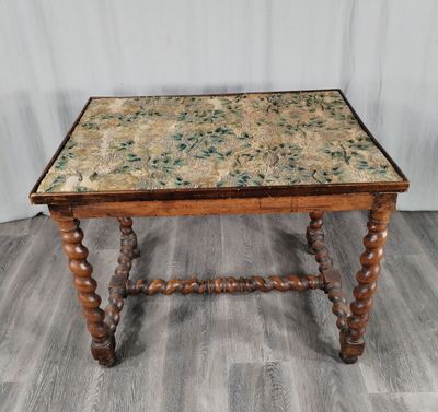 une vieille table en bois avec un plateau à motifs floraux et des pieds tournés