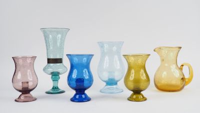 plusieurs vases en verre de différentes couleurs sont alignés sur une surface blanche