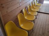 Dans une pièce, des chaises jaunes sont alignées contre un mur en bois