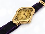 a gold wrist watch with a purple band on a white surface
