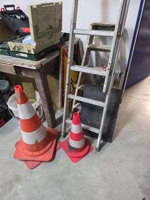 une échelle appuyée contre un mur, à côté d'une pile de cônes de signalisation