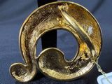 a gold brooch on a black stand with a tag on it