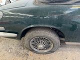 a dirty green car parked in a lot with other cars in the background