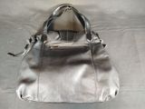 silver leather handbag on a bed with a white sheet